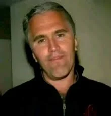 A man in a black jacket is standing in front of a wall