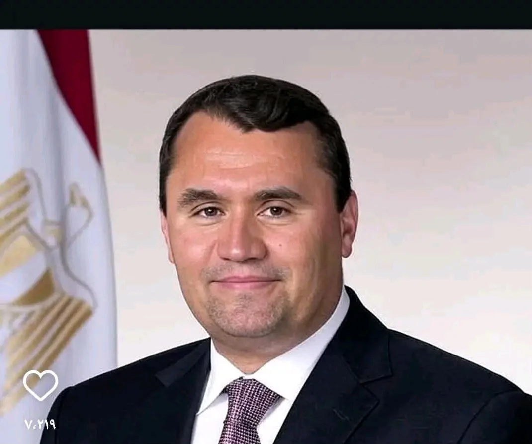A man in a suit and tie is standing in front of a flag