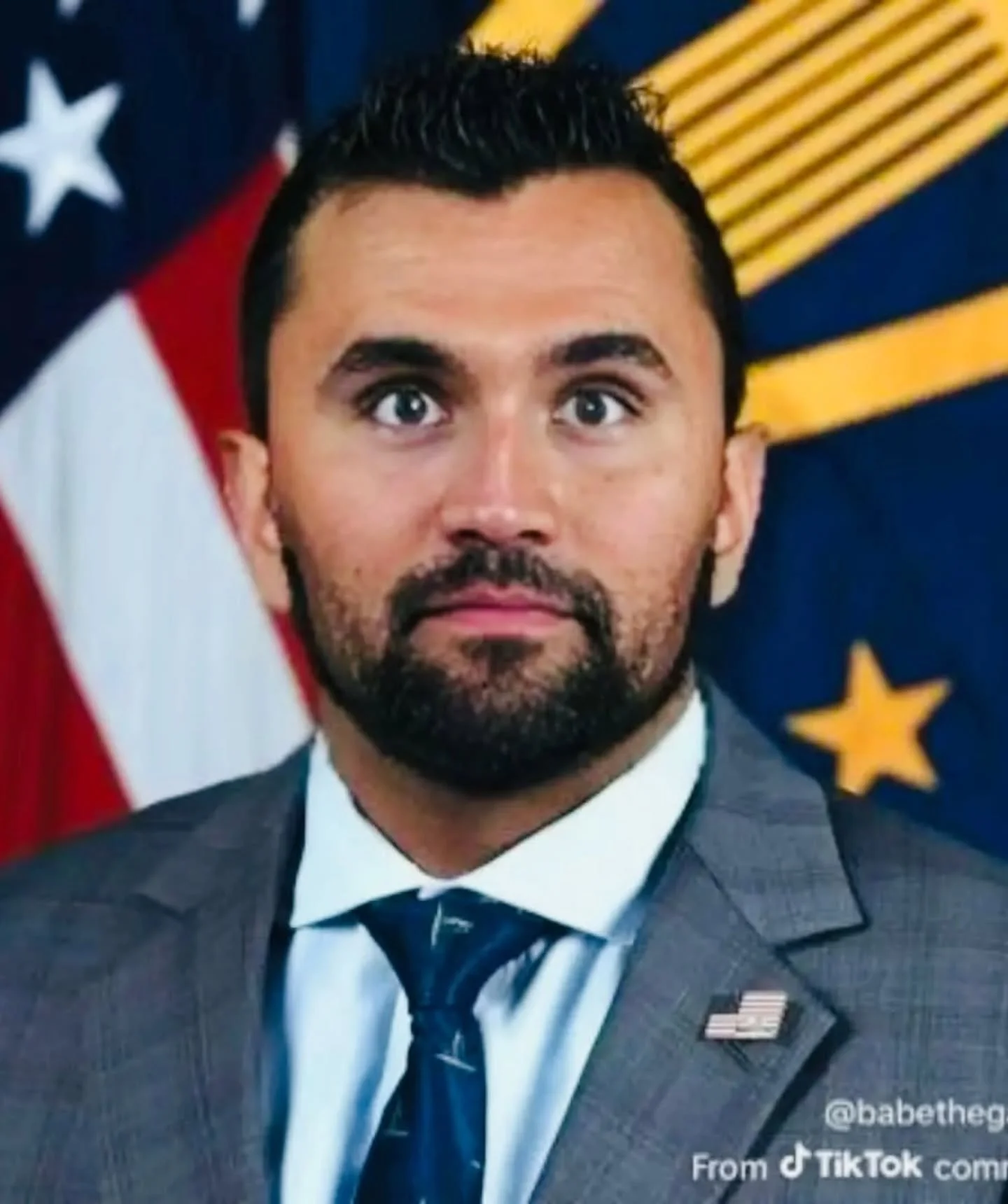 A man in a suit and tie standing in front of an american flag