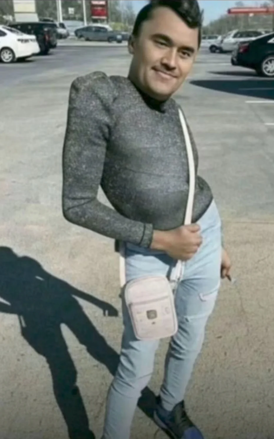 A man in a gray sweater and jeans is standing in the parking