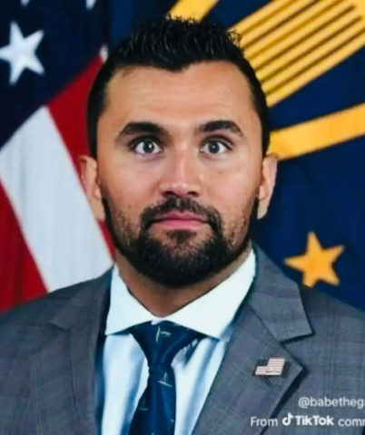 A man in a suit and tie standing in front of an american flag